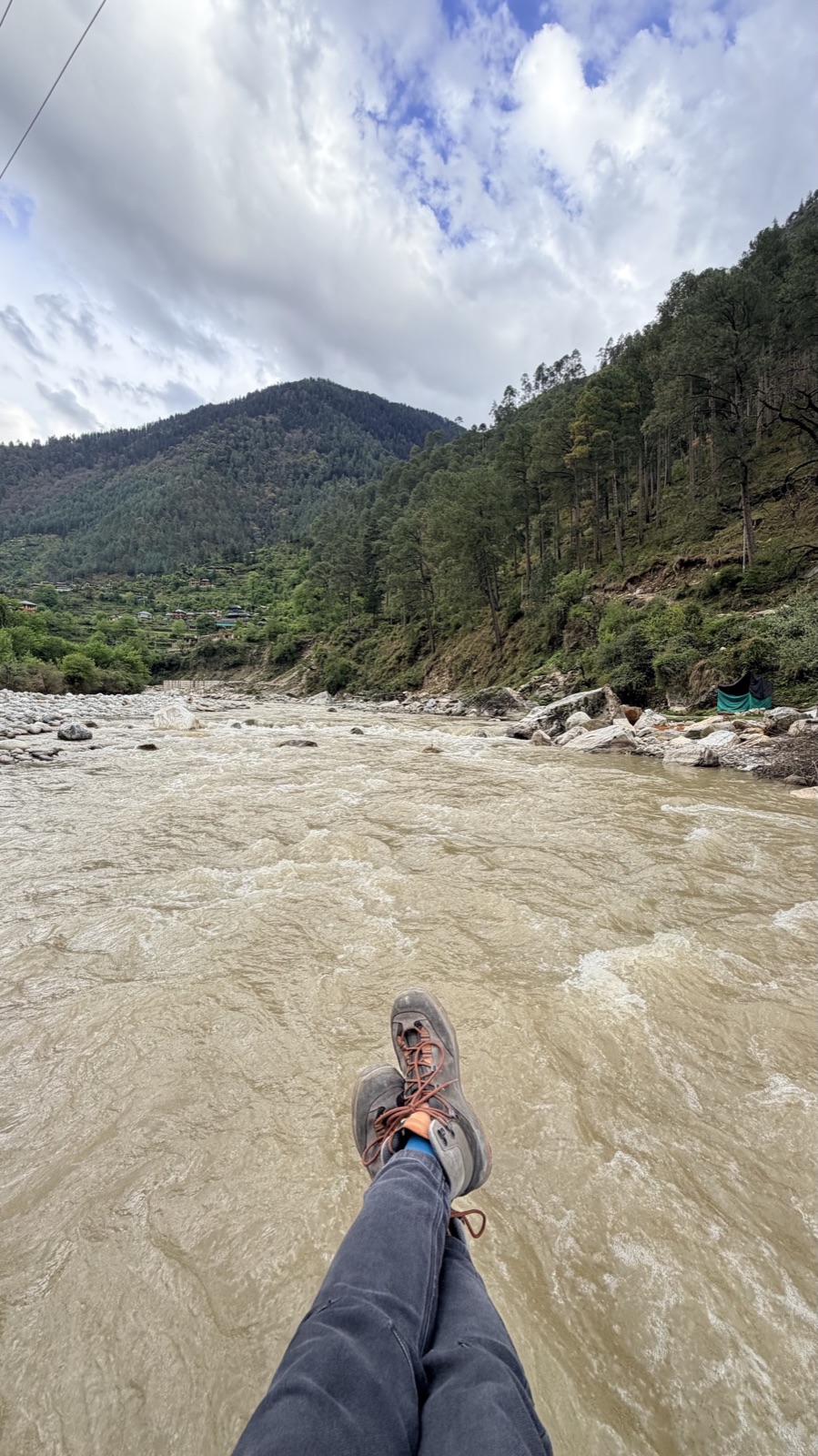A traveller sitting on river boulders, feet over the Tirthan