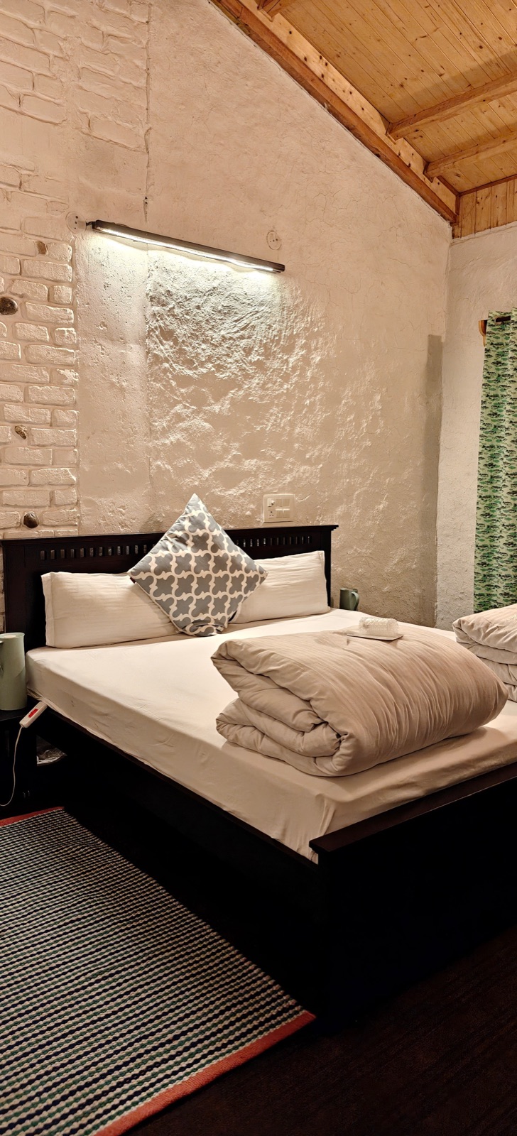 A bedroom at the Tirthan stay — stone walls, wooden ceiling, white bedding