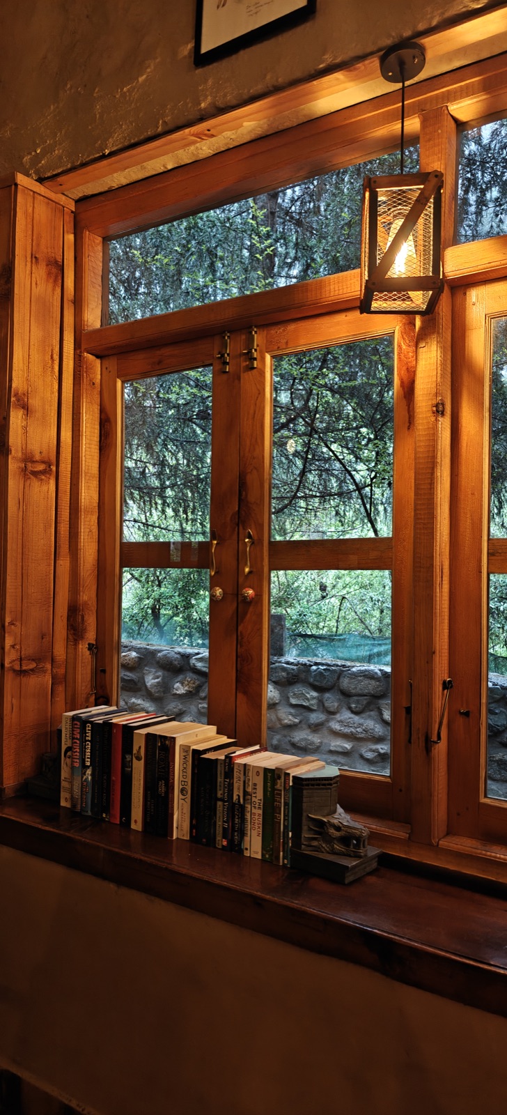 Books on a windowsill at the stay, an amber lantern glowing, trees through the glass