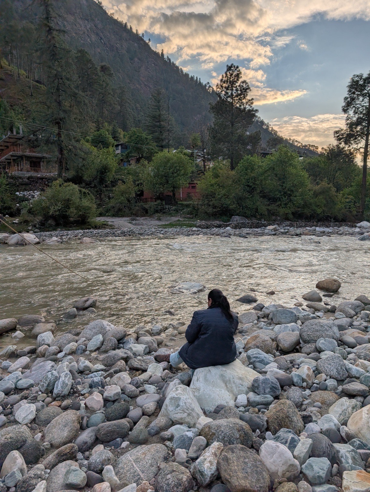 A traveller sitting by the Tirthan river at dusk