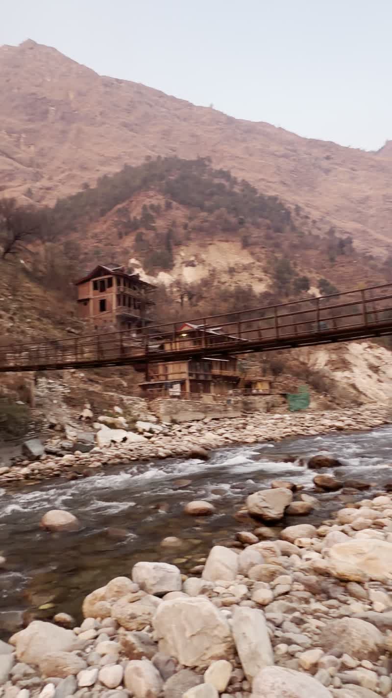 A bridge over the Tirthan river beneath a hazy sky